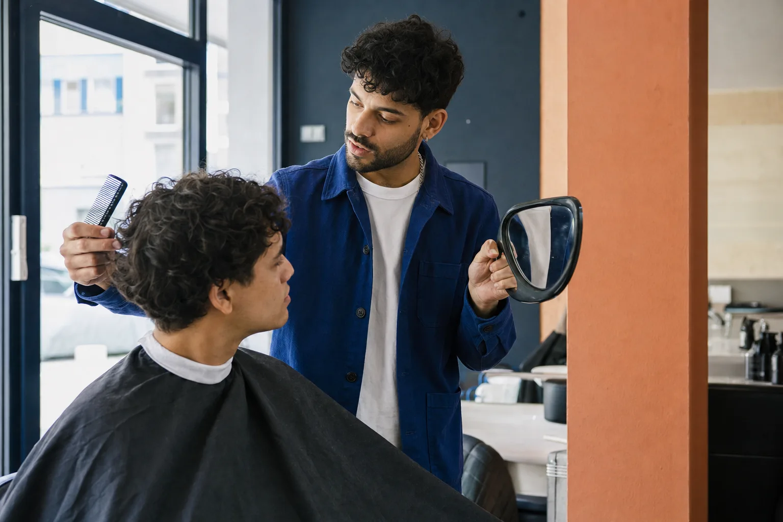Kapper bekijkt met een kam en handspiegel hoe het haar van een klant valt