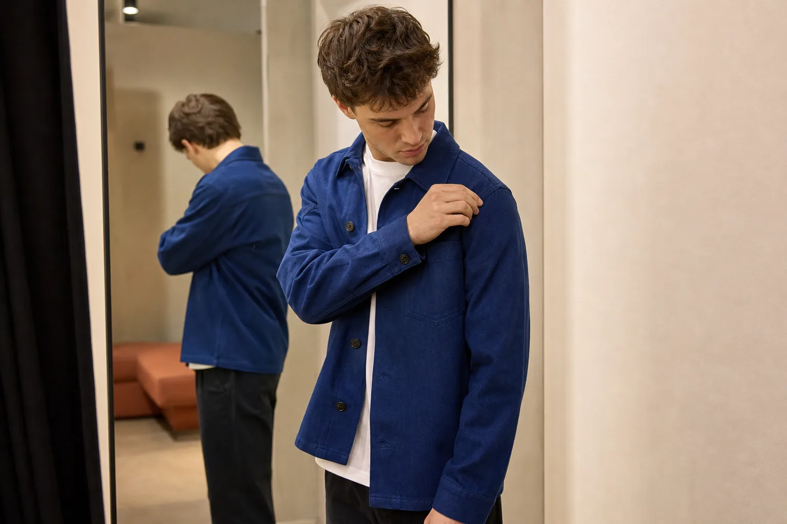 Jongvolwassene controleert de schoudernaad van een kobaltblauw overshirt in een paskamer